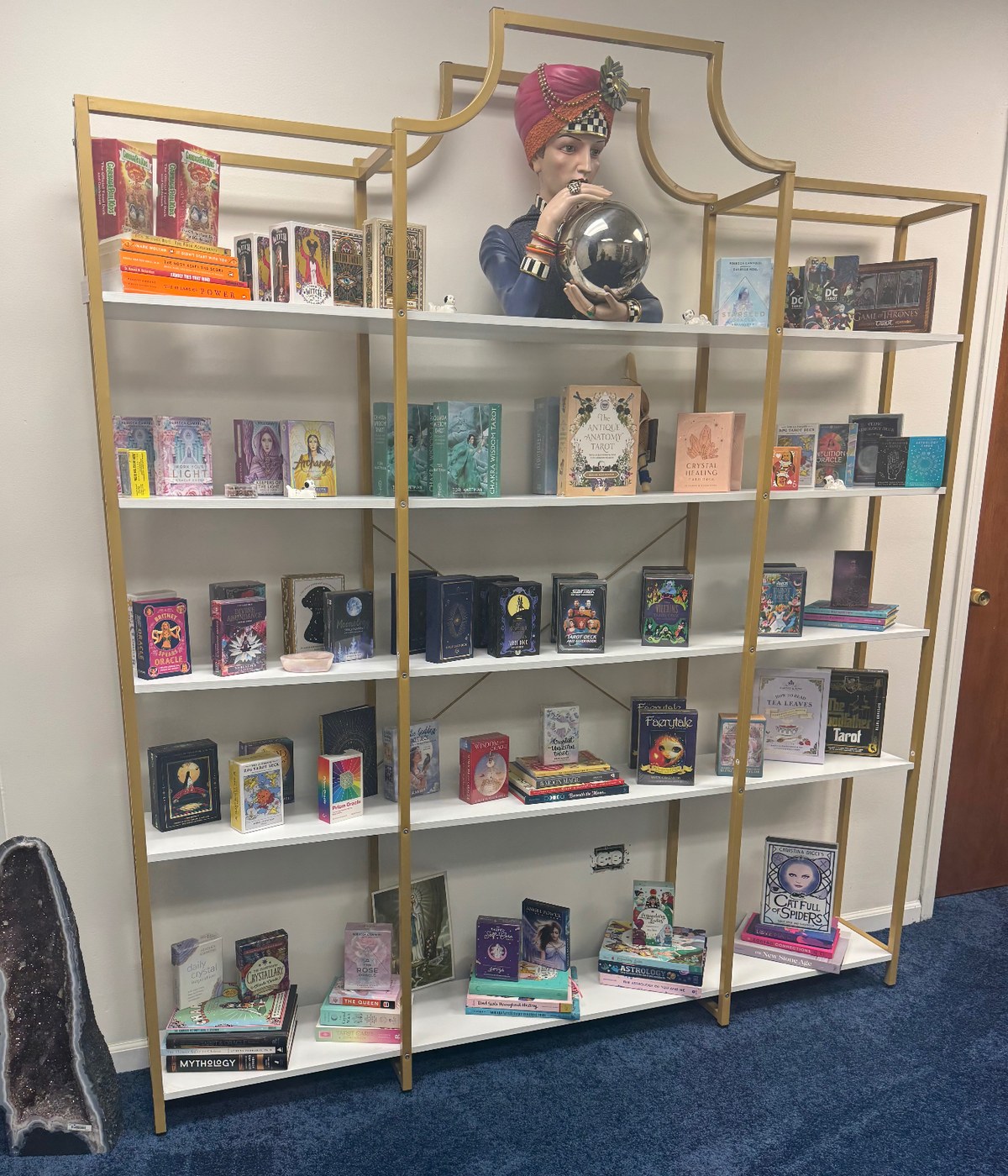 Tall gold shelf filled with tarot and oracle decks and spiritual books